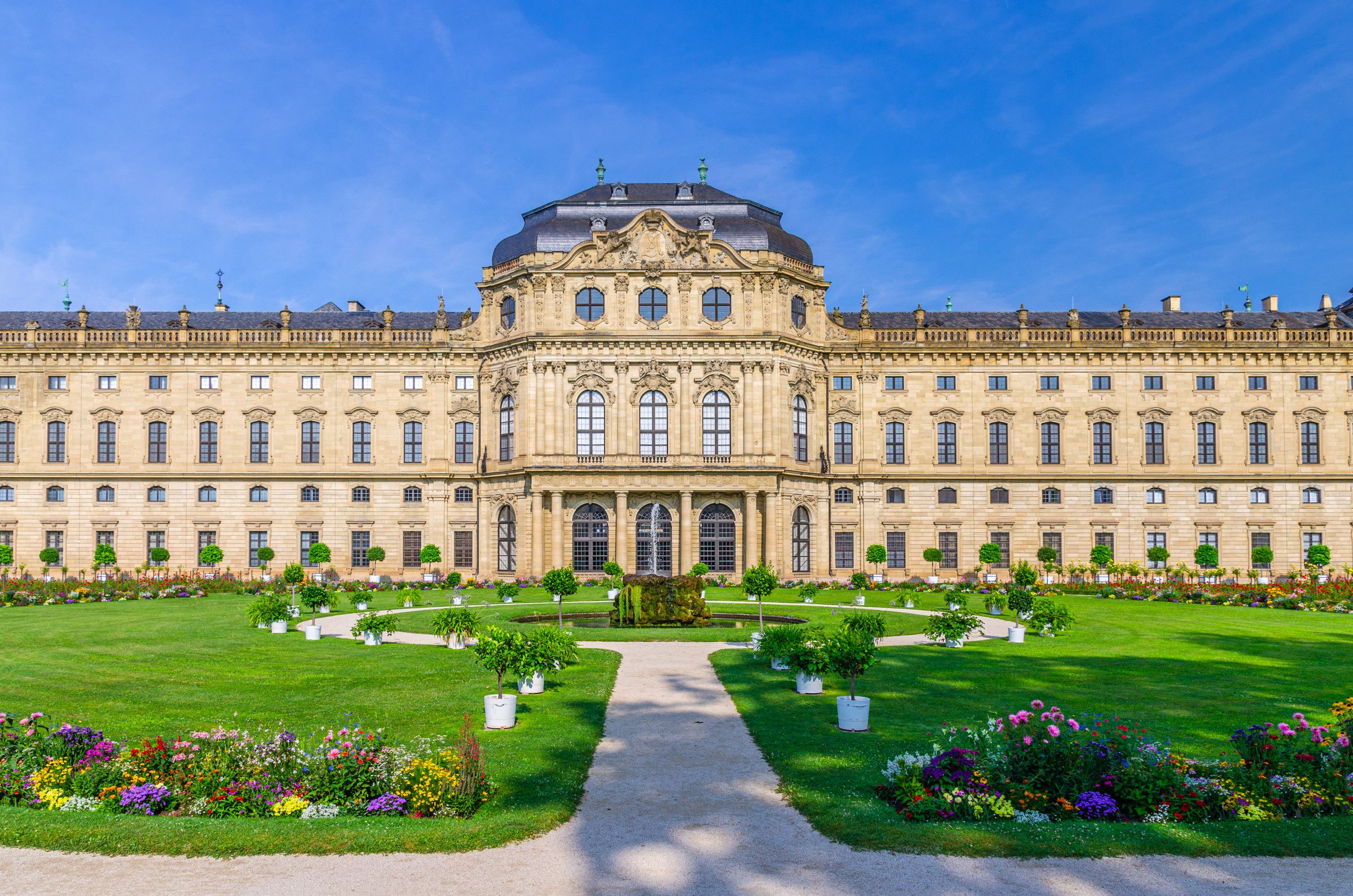 德國維爾茨堡官邸 (Würzburg Residence) 的主立面,一座巴洛克風格的宮殿,前方是修剪整齊的綠色草坪和花園,晴空萬里。