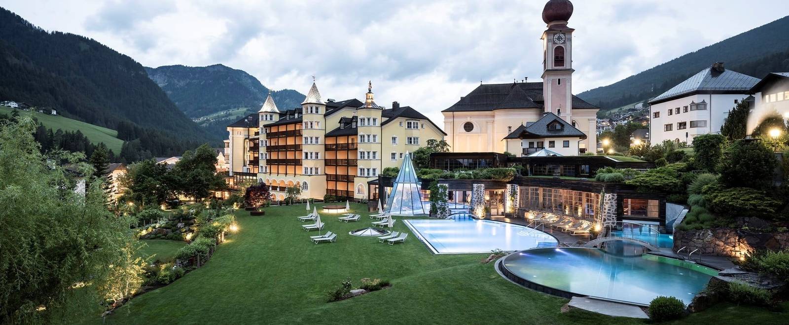 ADLER Spa Resort DOLOMITI 傍晚的庭園、泳池與村中教堂