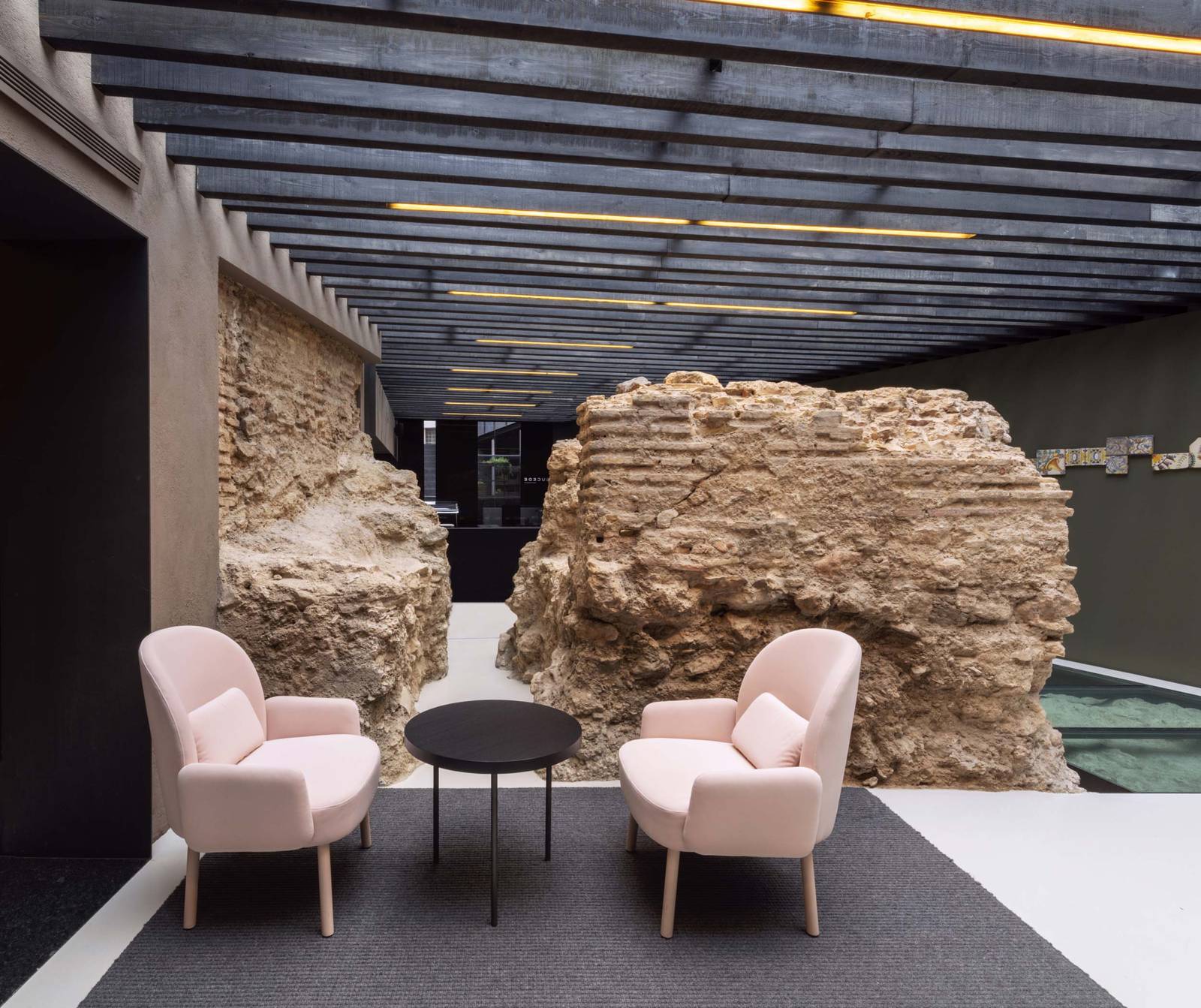 瓦倫西亞 Caro Hotel 館內保存的古老石牆遺跡與粉色扶手椅