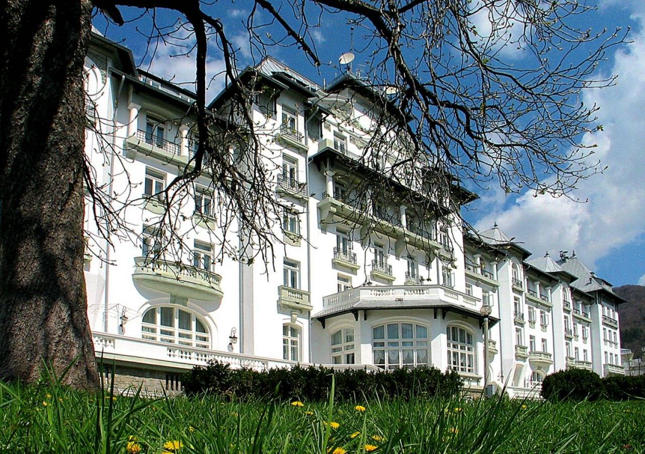 錫納亞 Hotel Palace 春天草地與老樹下的飯店立面